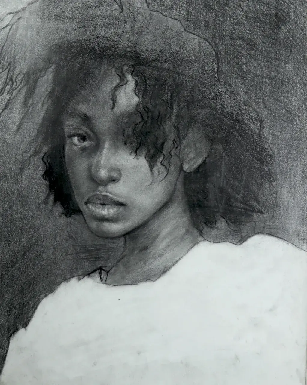 Charcoal portrait of a young girl looking forward from a softly shaded background.